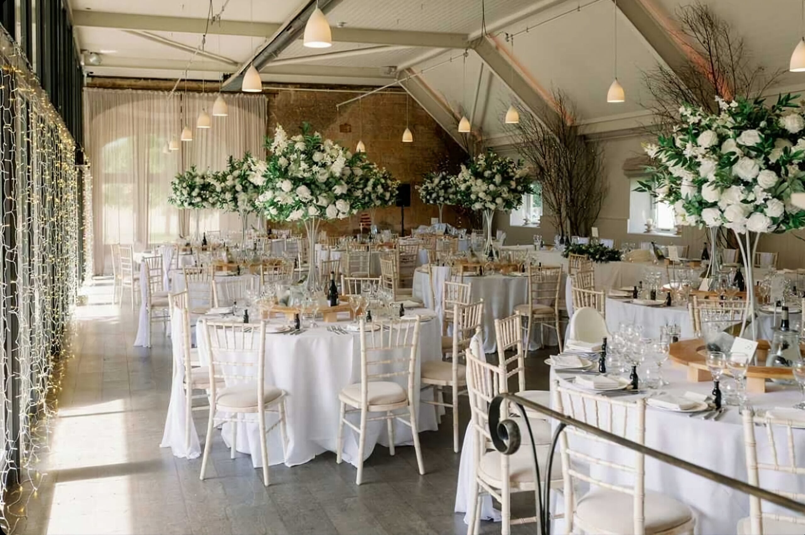 Round tables decorated with tall flower arrangements, waiting for guests to arrive for the wedding breakfast